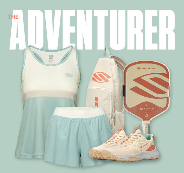 Selkirk "The Adventurer" pickleball collection in a sage-green and coral palette, featuring a colorblock racerback tank, light blue shorts, a cream crossbody sling bag, a terracotta Omni paddle, and matching cream-and-coral court shoes.
